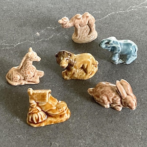 May include: A collection of small ceramic animal figurines, including a giraffe, camel, lion, elephant, rabbit, and a boot. The figurines are in various shades of brown, tan, and blue, with detailed features.