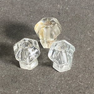 May include: Three clear glass cabinet knobs with a faceted design. The knobs have a hexagonal shape and are made of clear glass.