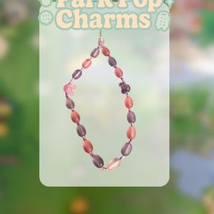 May include: A beaded phone charm with a variety of oval-shaped beads in shades of pink, brown, and gray. The charm includes small flower-shaped accents and the text "Park Pop Charms" in a light green font.