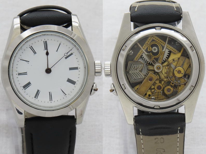 May include: A silver-toned wristwatch with a white face and black Roman numerals. The watch has a black leather band. The back of the watch is transparent, revealing the intricate mechanical workings of the timepiece.