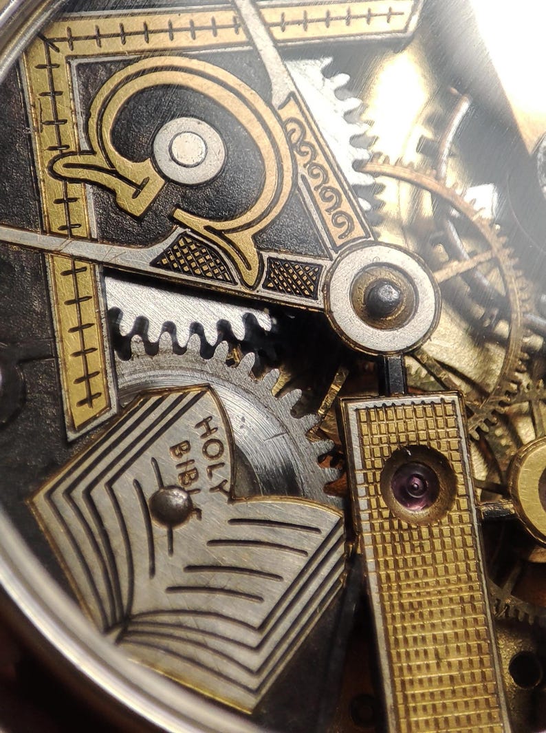 May include: Close-up of a vintage watch mechanism with intricate details. The design features gold and silver accents, gears, and the text "HOLY BIBLE" on a small book. The watch has a complex, layered appearance.