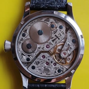 May include: A silver pocket watch with a black leather band. The back of the watch is open, revealing the intricate inner workings of the watch.