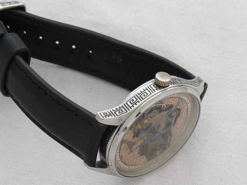 May include: A silver wristwatch with a black leather band. The watch face has a skeleton design with a gold-toned background.