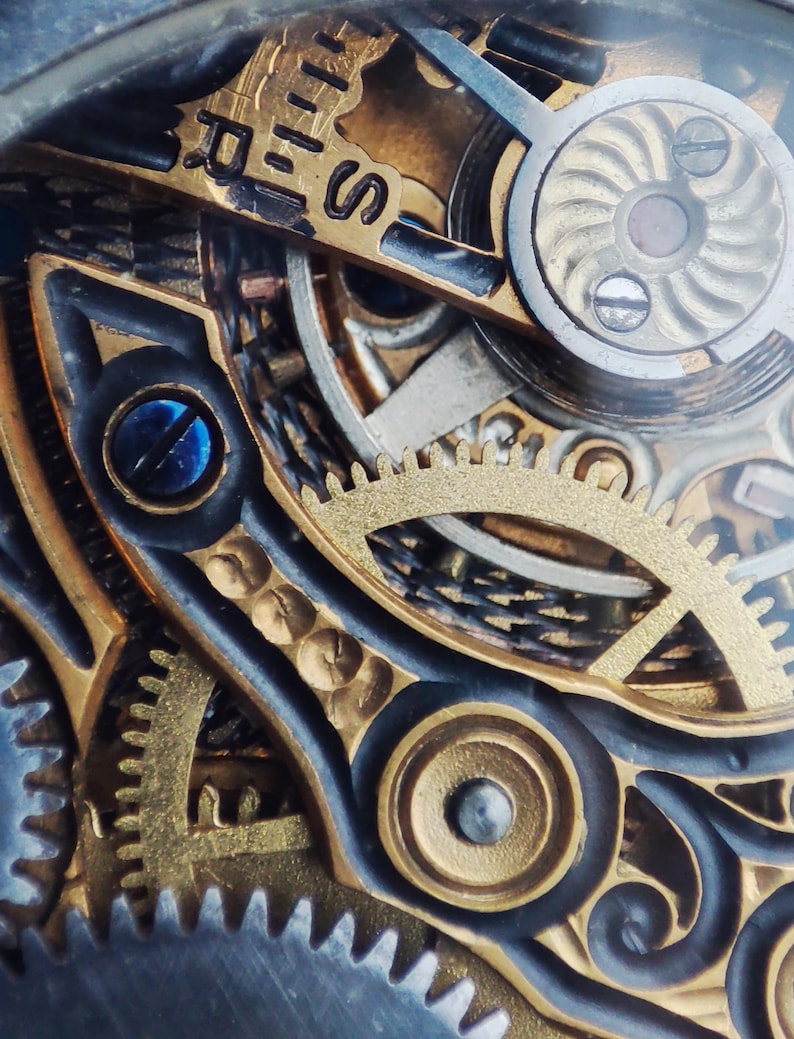 May include: Close-up of a complex watch mechanism with intricate gears and a gold-toned finish. The gears are visible through a clear glass cover, revealing the inner workings of the watch.