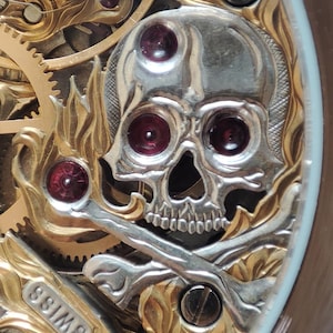 May include: Close-up of a gold and silver watch face with a skull and crossbones design. The skull has red jewels for eyes and the watch face says "Swiss".