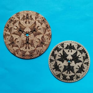 May include: Two circular discs featuring an intricate tessellated pattern of winged creatures. The larger disc is a warm copper tone with dark engraved details, while the smaller disc is silver-toned with black engraved details and a dotted border.