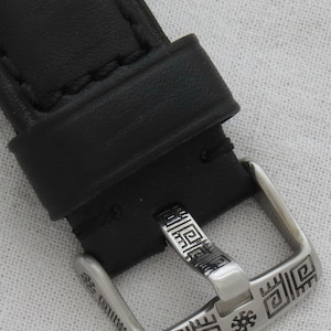 May include: A black leather watch strap with a silver buckle. The buckle has a geometric design with a small star in the center.