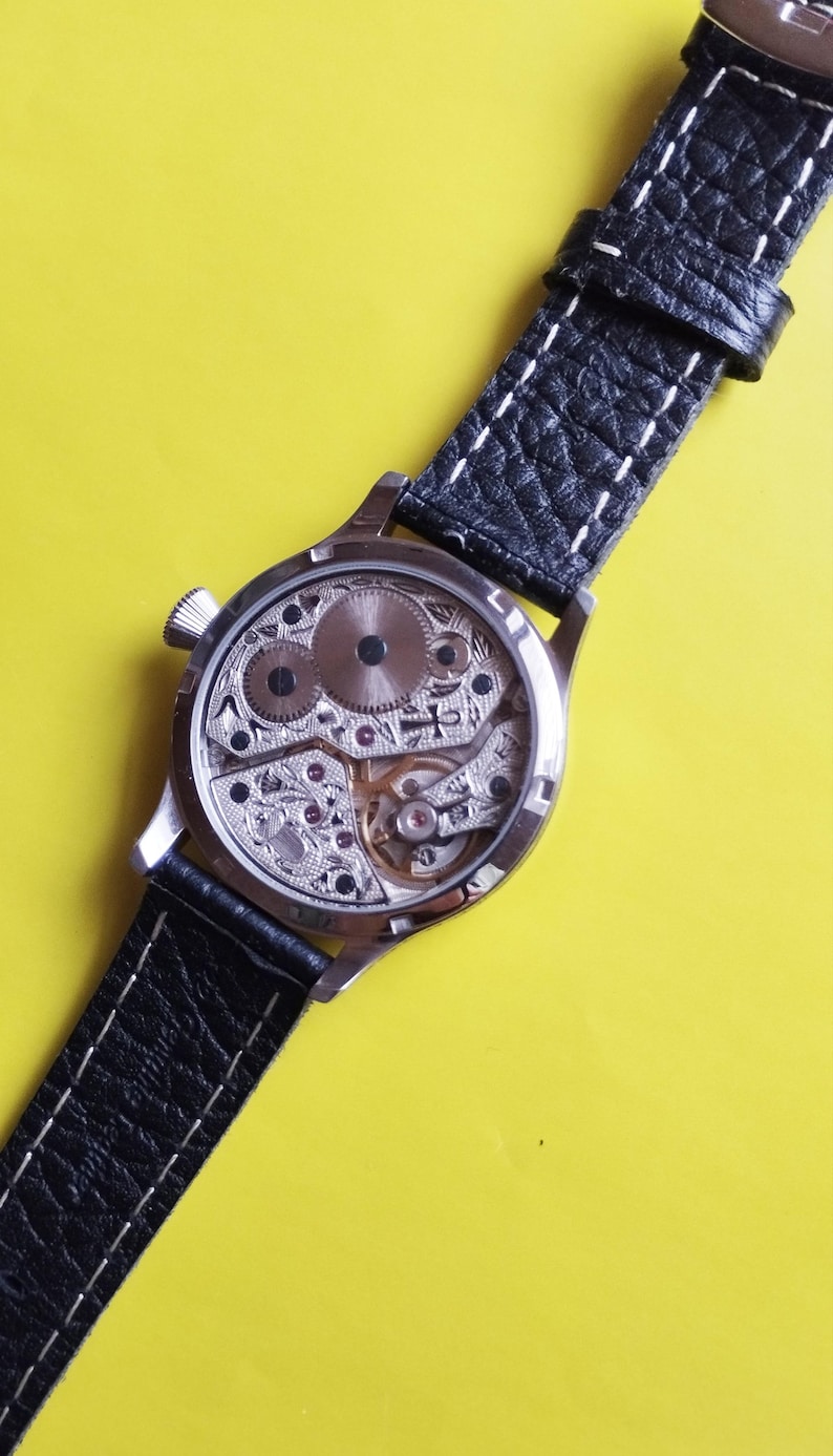 May include: A silver wristwatch with a black leather band and a clear back revealing the inner workings of the watch.