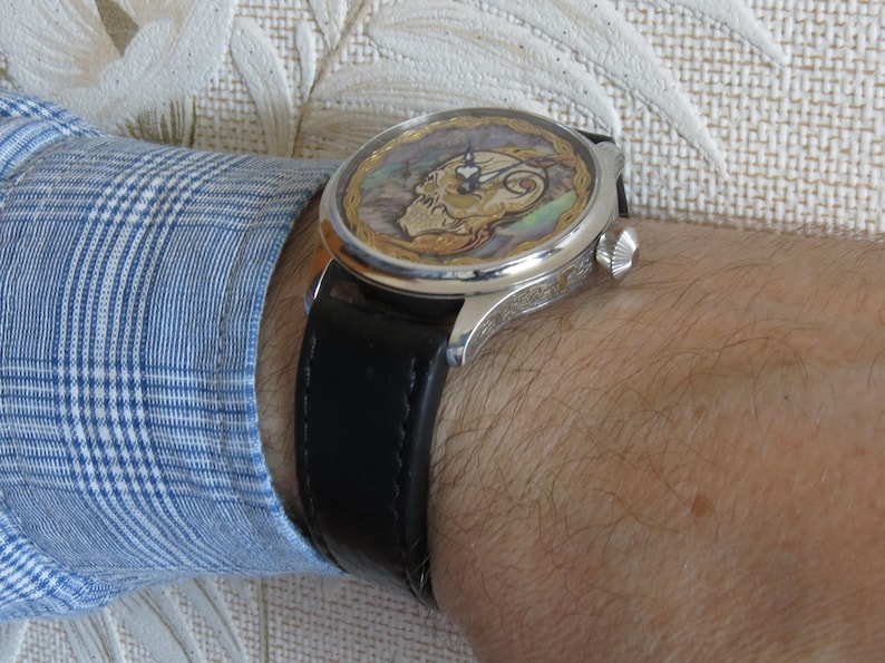 May include: A silver wristwatch with a black leather band. The watch face features a colorful, detailed design.