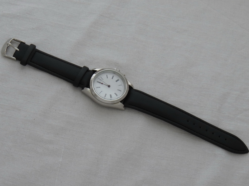 May include: A wristwatch with a black leather band and a silver-colored case. The watch face is white with black hour markers and hands. The band is secured with a silver buckle.