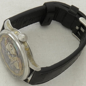 May include: A silver pocket watch with a black leather band. The watch face has a detailed, colorful design with gold accents.