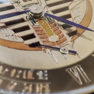 May include: Close-up of a watch face with a gold and black design. The face features a skull with a pharaoh's headdress and Roman numerals around the edge.