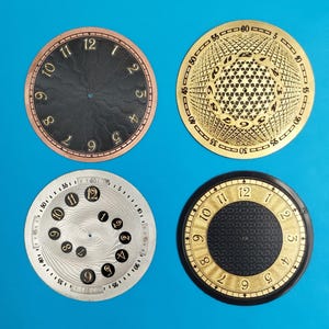 May include: Four watch faces with different designs. One is black with gold numerals, another is silver with black numerals, and two are gold-coloured with black numerals. The faces are circular and have a variety of textures and patterns.
