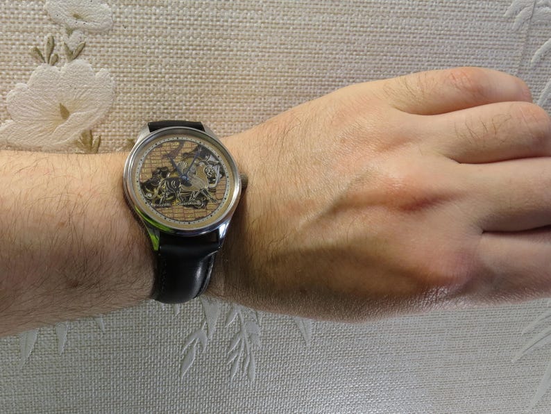 May include: A silver wristwatch with a black leather band. The watch face has a skeleton design with a gold-toned background and intricate details.