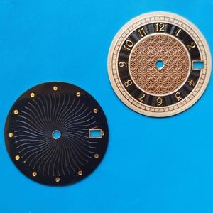 Peut inclure: Deux cadrans de montre sur fond bleu. L'un est noir avec un motif en spirale et des accents dorés. L'autre est doré et noir avec des chiffres dorés et un centre à motifs. Les deux ont une petite ouverture rectangulaire.