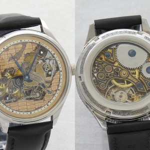 May include: A silver skeleton watch with a black leather band. The watch face features a detailed, intricate design of a bird in flight. The back of the watch reveals the inner workings of the movement.