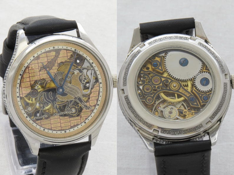 May include: A silver skeleton watch with a black leather band. The watch face features a detailed, intricate design of a bird in flight. The back of the watch reveals the inner workings of the movement.