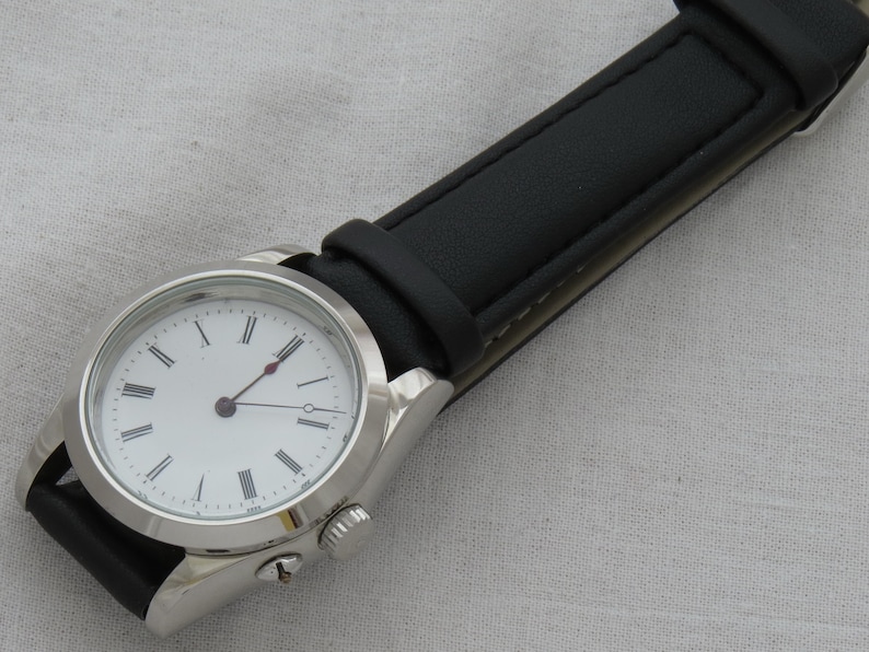 May include: A silver wristwatch with a white face and black Roman numeral hour markers. The watch has black hands and a black leather band. The watch case is approximately 1.5 inches in diameter.