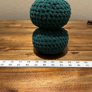 May include: Two teal green crocheted balls stacked on top of each other on a wooden surface.