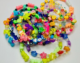 May include: A collection of colorful beaded bracelets with various charms, including smiley faces, stars, and cartoon animals. The bracelets are made with clear, iridescent, and opaque beads.
