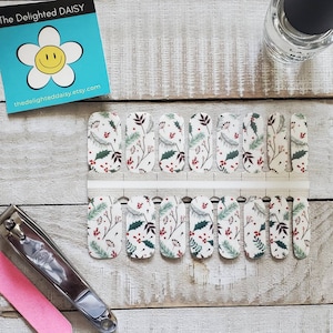May include: Nail wraps with a white background, featuring a pattern of green leaves, red berries, and brown branches. A bottle of clear nail polish, nail clippers, and a pink nail file are also visible. The Delighted Daisy etsy.com logo is in the top left.