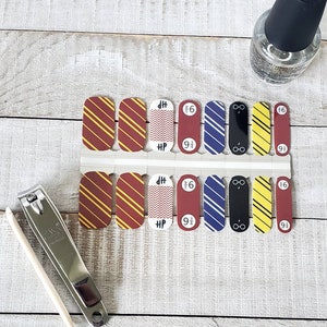 Può includere: Un set di 12 nail wraps con design a tema Harry Potter. I design includono un motivo a strisce rosso e oro, un motivo a chevron, un motivo a strisce blu e bianco, un paio di occhiali e un motivo a strisce giallo e oro. Le nail wraps sono disposte in due file da sei.
