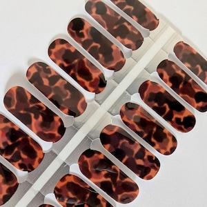 May include: Nail art strips with a tortoiseshell pattern. The strips are a mix of dark brown, reddish-brown, and amber colors. The nail art strips are arranged in rows on a clear backing.