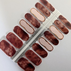 May include: A sheet of nail polish wraps with a marbled design in shades of brown and pink. The wraps have a gold accent around the edges.