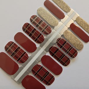 Pode incluir: Uma folha de envoltórios de esmalte de unhas com uma base bordô e um padrão xadrez em preto e dourado. A folha também inclui envoltórios de glitter dourado sólido.