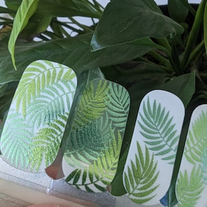May include: Four white nail wraps with a green tropical leaf design. The leaves have a glittery texture.