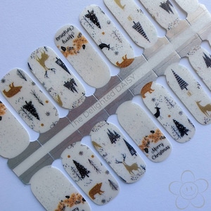 Könnte beinhalten: Eine weiße Folie mit Nagellack-Wraps im Winterwald-Design. Die Wraps zeigen verschiedene Motive, darunter Bäume, Hirsche, Bären und Schneeflocken. Der Text "Merry Christmas" ist auf einem der Wraps abgebildet.