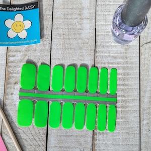 Könnte beinhalten: Eine Folie mit grünen Nagellack-Wraps mit einem grauen und grünen Rand. Die Wraps sind in zwei Reihen zu je zehn angeordnet. Der Text "The Delighted Daisy" ist auf einem blauen Aufkleber sichtbar.