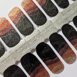 Puede incluir: Tiras de esmalte de uñas con un diseño degradado. Las tiras transicionan de un dorado brillante a un negro oscuro, con una capa marrón intermedia. Las tiras están dispuestas en filas y listas para ser aplicadas.