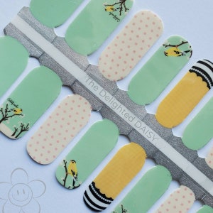 May include: A sheet of nail wraps with a green, yellow and white design. The design features a small bird, polka dots and the text "The Delighted Daisy".