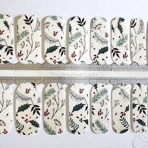 May include: Nail wraps with a cream background and a repeating pattern of green holly leaves, dark red berries, and brown sprigs. The nail wraps are arranged in rows and are ready to apply. The text "The Delighted Daisy" is visible.