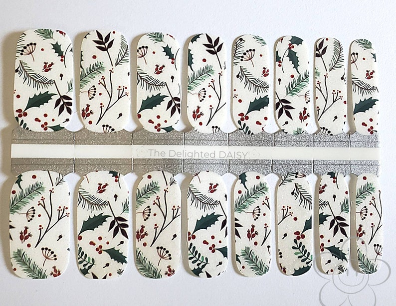 May include: Nail wraps with a cream background and a repeating pattern of green holly leaves, dark red berries, and brown sprigs. The nail wraps are arranged in rows and are ready to apply. The text "The Delighted Daisy" is visible.