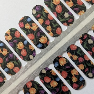 May include: Nail wraps with a floral design featuring colourful tulips on a black background. The wraps are arranged on a silver and white backing.