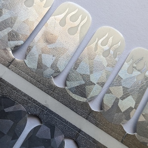May include: A sheet of nail decals with a silver holographic finish. The decals feature a flame design in white.