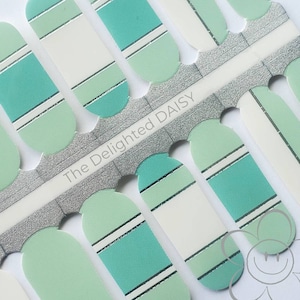 May include: Nail polish wraps with a teal and green striped design. The wraps are packaged on a silver sheet with the text "The Delighted Daisy".