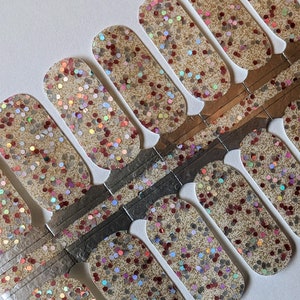 May include: A set of nail wraps with a gold glitter and red glitter design. The wraps are arranged in a fan shape on a white background.
