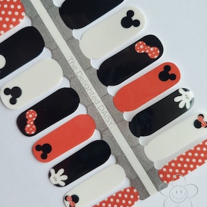 May include: A sheet of nail polish wraps featuring a Mickey Mouse theme. The wraps have a red, black and white colour scheme with polka dots, Mickey Mouse ears and a bow. The wraps are labelled "The Delighted Daisy".