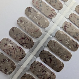 May include: A sheet of nail polish wraps with a floral pattern in shades of brown, white, and pink. The wraps are designed to be applied to fingernails.
