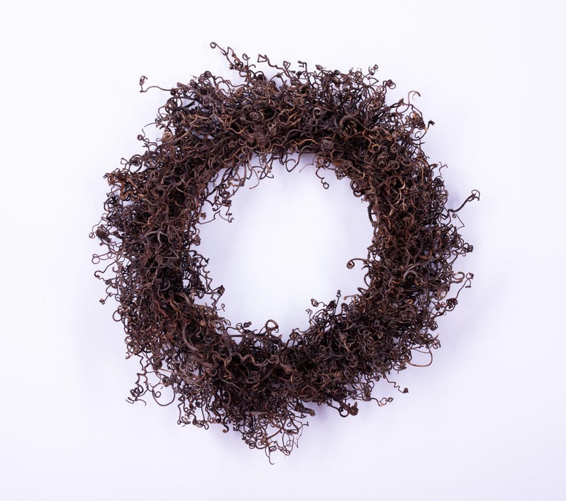 May include: A circular wreath composed of dried, curly brown twigs, set against a white background. The twigs are densely packed, creating a textured, natural appearance. This decorative wreath is suitable for seasonal home decor.