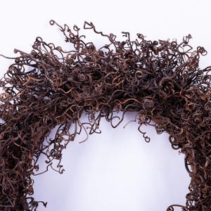 May include: A decorative wreath made from tightly curled, dried brown vines. The wreath is arranged in a circular shape, with the curly vines densely packed together. The background is a plain white surface.