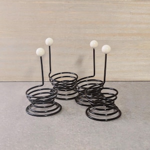 Könnte beinhalten: Drei schwarze Metalleierhalter mit weißen Keramikspitzen. Jeder Halter ist ein Spiralfederdesign.