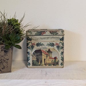 Peut inclure: Boîte en étain vintage avec un motif floral vert, rouge et blanc. La boîte présente une image d'un château avec le texte "ELISEN Nürnberger Lebkuchen".