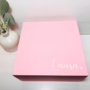 May include: A pink gift box with the name "Laura" written in white on the top.