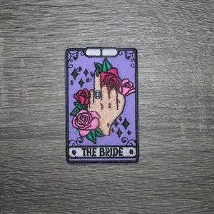 May include: Purple tarot card with a hand holding a rose and the text "The Bride".