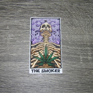 Peut inclure: Un patch blanc avec un squelette fumant un joint, entouré de fumée violette. Le texte "THE SMOKER" est en bas du patch.