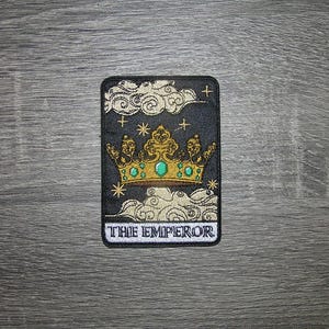 May include: Embroidered patch featuring a gold crown with green accents, set against a dark background with clouds and stars. The text "THE EMPEROR" is displayed at the bottom. The patch is rectangular with rounded corners.